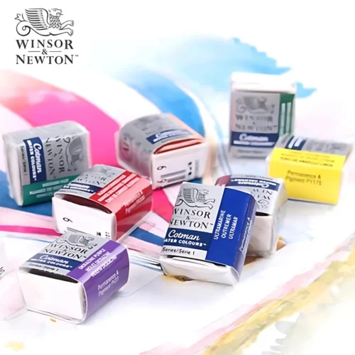 There are 8 Winsor and Newton Cotman Half Pans shown randomly in the center of the frame. Each pan is square in shape and sealed with a wrapper. Each pan has a colour band printed on it to show the colour of the paint. They are laying on a piece of paper that has some watercolour painted on it randomly. The Winsor and Newton logo is shown in the top left hand corner of the frame.