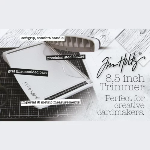 A promotional image for the Tim Holtz Guillotine Trimmer. The trimmer has a light grey plastic base and a guillotine arm with a black kushgrip handle for comfort. The Tim Holtz logo is shown in the image.