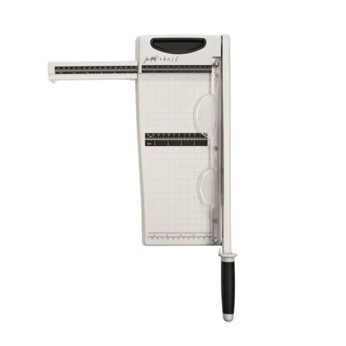 The Tim Holtz Maxi Guillotine Comfort Paper Trimmer has a light grey plastic base with grid marks debossed on the surface. It has a imperial and metric rulers with an extendable base and a geared rotary trimmer arm. The extendable arms are shown pulled out. The trimmer is rectangular in shape and is shown in the frame at a slight angle on a white background.