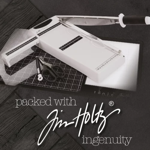 A promotional image for the Tim Holtz Maxi Guillotine Comfort Paper Trimmer. The trimmer has a light grey plastic base and a guillotine arm with a black kushgrip handle for comfort. The Tim Holtz logo is shown in the image. On a dark grey background.