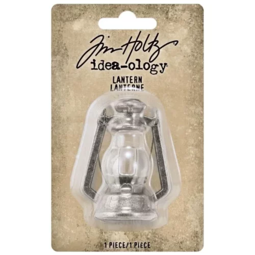 A single pack of Tim Holtz Idea-ology Lantern is shown in the center of the frame. The pack has a brown, distressed, printed backing board and a clear, molded plastic top that holds the products inside the packaging. The Tim Holtz logo is printed at the top of the pack. The pack has a hole at the top so that it is able to hang. You can see the items through the clear, molded plastic top. The image is center of the frame and on a white background.