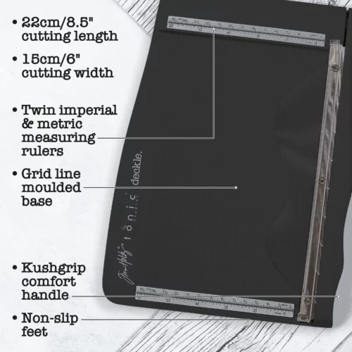 A promotional image for the Tim Holtz Deckle Torn Edge Trimmer. The trimmer has a black plastic base and a guillotine arm with a black kushgrip handle for comfort. The Tim Holtz logo is shown in the image. On a dark grey background.