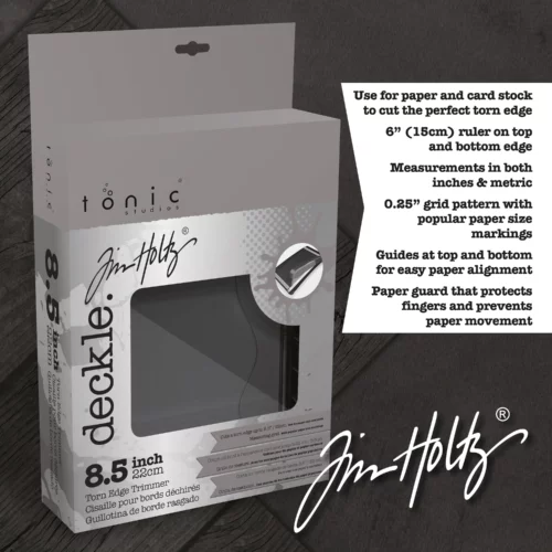 A promotional image for the Tim Holtz Deckle Torn Edge Trimmer. The trimmer has a black plastic base and a guillotine arm with a black kushgrip handle for comfort. The Tim Holtz logo is shown in the image. On a dark grey background.