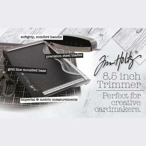 A promotional image for the Tim Holtz Deckle Torn Edge Trimmer. The trimmer has a black plastic base and a guillotine arm with a black kushgrip handle for comfort. The Tim Holtz logo is shown in the image.