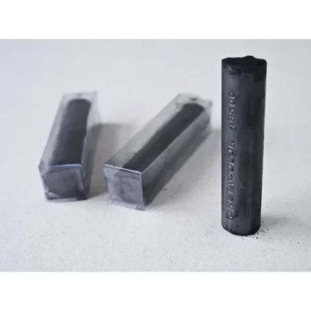 there are trhee cretacolor chunky charcoal sticks. one on the far right is standing vertical. the two on the left are lying down. there are shadows casting off of them. the two lying down are in plastic containers. the one standing up has the name of the products etched into it.