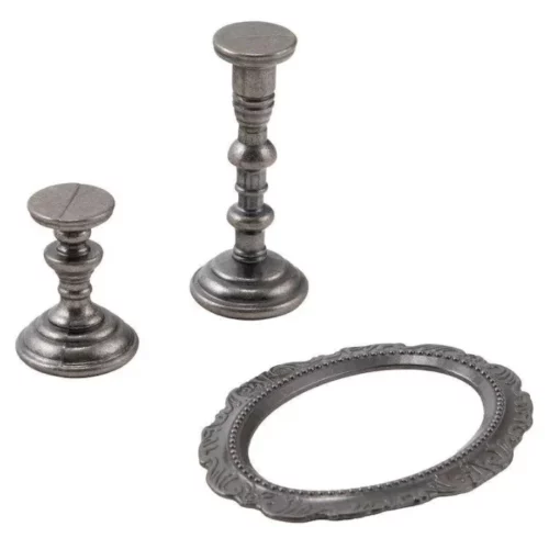 A close up of the contents of a pack of Tim Holtz Idea-ology The Manor. There are two ornate metal candlesticks at the top left hand corner of the frame and an ornate, metal, oval frame laying down at the front of the frame. The image is center of teh frame and on a white background.