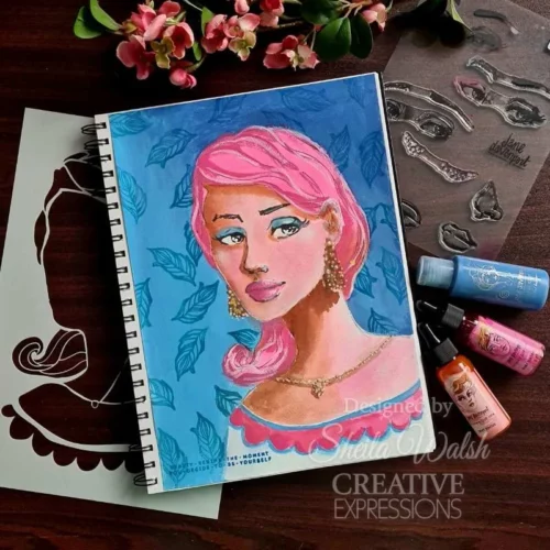 A project, that was made using the Facetime Features Jane Davenport Creative Expressions Clear Stamp Set can be seen in the frame. The image is of a sketch pad that has a womans face stamped onto it and coloured in with a blue background.