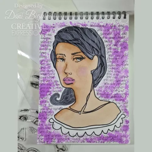 A project, that was made using the Facetime Features Jane Davenport Creative Expressions Clear Stamp Set can be seen in the frame. The image is of a sketch pad that has a womans face stamped onto it and coloured in with a purple background.