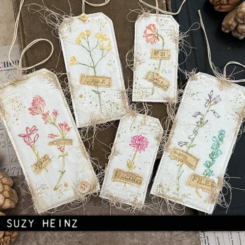 6 tags are shown in the frame that were made using the Forgotten Garden Tim Holtz Stamp Set. The tags are vintage themed and have thin rope threaded through each tag.