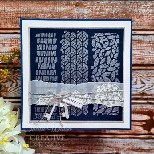 A card is shown in the frame that was made using the Mezzo Woodware Stencil. The background is blue with the stencil design on top using silver embossing powder.