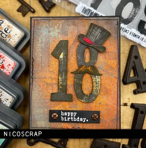 A card is shown in the frame that was made using the Paint By Number Tim Holtz Stamp Set. The card is vintage themed and has numbers printed on the front.