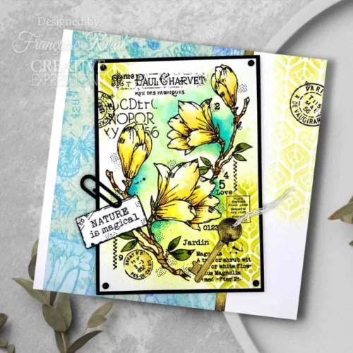 A greeting card that was made using the Spring Magnolia Woodware Clear Stamp Set is shown in the frame. The card is blue and yellow and the flowers have been coloured in yellow too.