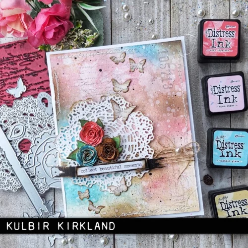 A card is shown in the frame that was made using the Vault Boutique by Tim Holtz Thinlits Die Set. The card front is soft coloured with a doily cutout and some flowers.