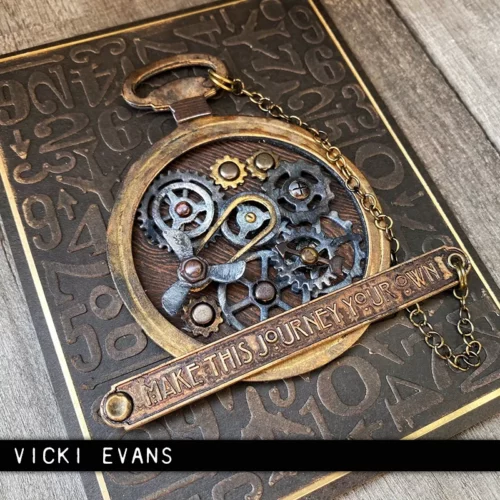A vintage style card is shown in the frame, which was made using the Vault Watch Gears by Tim Holtz Thinlits Die Set. There is a clock watch on the front of the card that is filled with loads of mini gears.