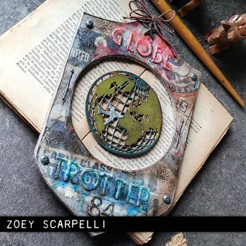An altered art panel is shown in the frame that was made using the Vault World Travel by Tim Holtz Thinlits Die Set. There is a world map in the center of the panel.