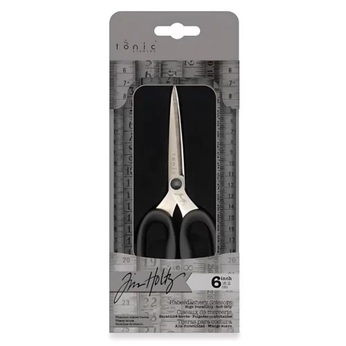 A pair of Tim Holtz Haberdashery Scissors can be seen in their tin which is laying vertically in the center of the frame. The tin has a clear lid so you can see the scissors inside. On a white background.