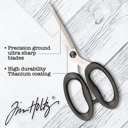 A promotional image for Tim Holtz Haberdashery Scissors. The scissors are shown laying on a faux wooden background. There are lines pointing to 2 parts of the scissors and black text describing those parts of the scissors. The Tim Holtz logo is seen in the top right hand corner of the frame.