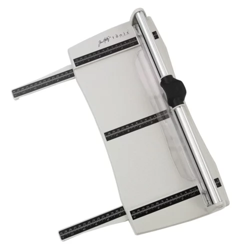 The Tim Holtz Rotary Media Trimmer has a light grey plastic base with grid marks debossed on the surface. It has a imperial and metric rulers with an extendable base and a geared rotary trimmer arm. The extendable arms are shown pulled out. The trimmer is rectangular in shape and is shown in the frame at a slight angle on a white background.