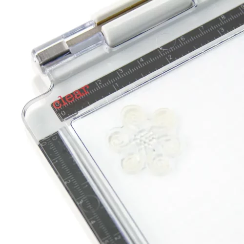 A close up of the a corner of the Tim Holtz Stamping Platform. The clear perspex lid is closed and there is a red word that indicates what stamp can be used on this side of the perspex lid. On a white background