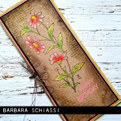 A single thin card that was made using the Embroidery Tim Holtz Stamp Set is shown in the center of the frame on a faux wooden background. The card is brown with flowers stamped on the front that have been coloured in with pinks and reds.