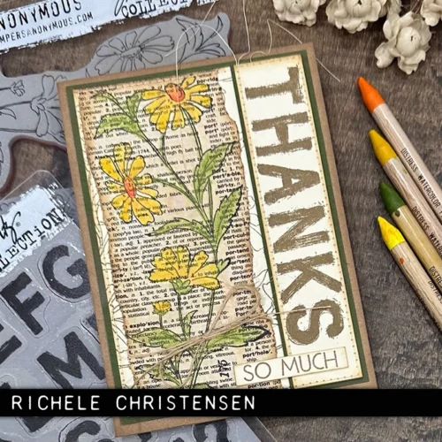 A single card that was made using the Embroidery Tim Holtz Stamp Set is shown in the center of the frame on a faux wooden background. The card is brown with flowers stamped on the front that have been coloured in with pinks and reds.