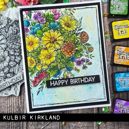 A card that was made using the Floristry Tim Holtz Stamp Set is shown vertically in the center of the frame. The flowers have been coloured in with a variety of different colours and the is a Happy Birthday greeting on black cardstock on the card cover. There are various mini ink pads scattered around the card along the right hand side of the frame. The image is cut off by the frame.