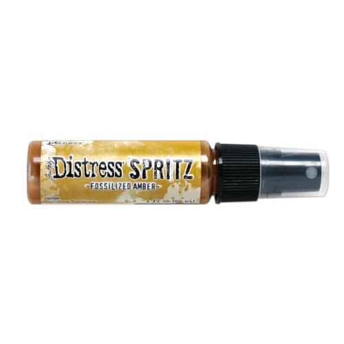 A single bottle of Fossilized Amber Tim Holtz Distress Spritz is shown laying horizontally in the center of the frame. The bottle is a clear plastic with a black plastic spray top and a clear plastic lid. There is a coloured label around the body of the bottle that indicates the colour of the ink. The Distress Logo and product details are printed on the label. The image is center of the frame and on a white background.