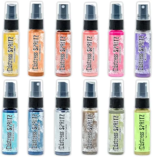 There are 12 bottles of Tim Holtz Distress Spritz shown in the frame. There are 2 rows and 6 bottles in each row. The bottles are a clear plastic with a black plastic spray top and a clear plastic lid. There is a coloured label around the body of each bottle that indicates the colour of the ink. The Distress Logo and product details are printed on the label. The image is center of the frame and on a white background.