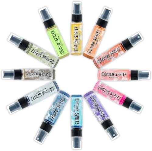 There are 12 bottles of Tim Holtz Distress Spritzes shown laying in a circle in the center of the frame on a white background. The bottles are a clear plastic with a black plastic spray top and a clear plastic lid. There is a coloured label around the body of each bottle that indicates the colour of the ink. The Distress Logo and product details are printed on the label.