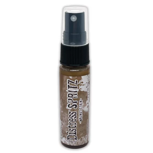 A single bottle of Walnut Stain Tim Holtz Distress Spritz is shown standing vertically in the center of the frame. The bottle is a clear plastic with a black plastic spray top and a clear plastic lid. There is a coloured label around the body of the bottle that indicates the colour of the ink. The Distress Logo and product details are printed on the label. The image is center of the frame and on a white background.