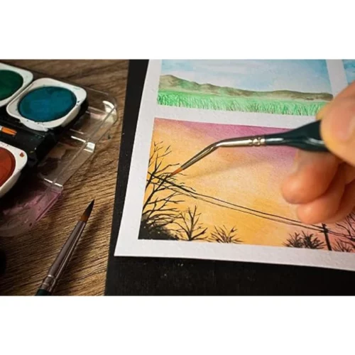 A close up of a persons hand that is coming in from the right hand side of the frame, holding a brush from the Mont Marte Fine Detail Brush Set. They are painting a fine line with the brush.