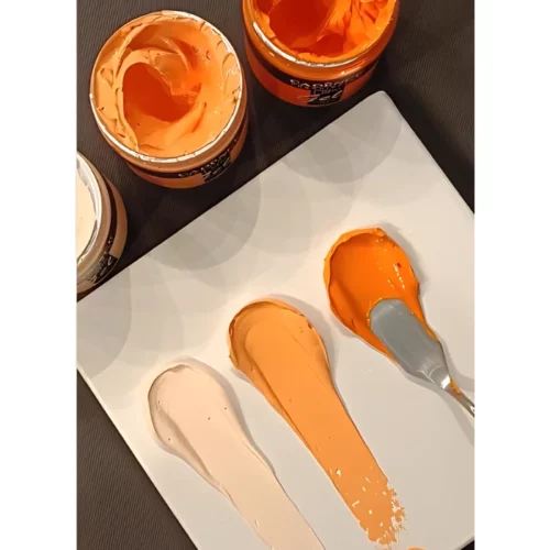 Cadence Connoissuer Heavy Body Gel Acrylic is shown being used on a piece of paper with a palette knife. various shades of orange are being used in the sample. they are showing the texture of the paint. on a wooden table background with three open pots of the paint behind it.